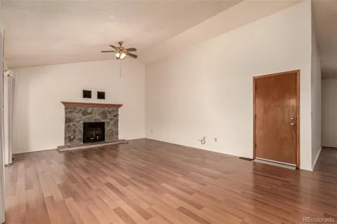 an empty room with wooden floor a ceiling fan a fireplace and windows