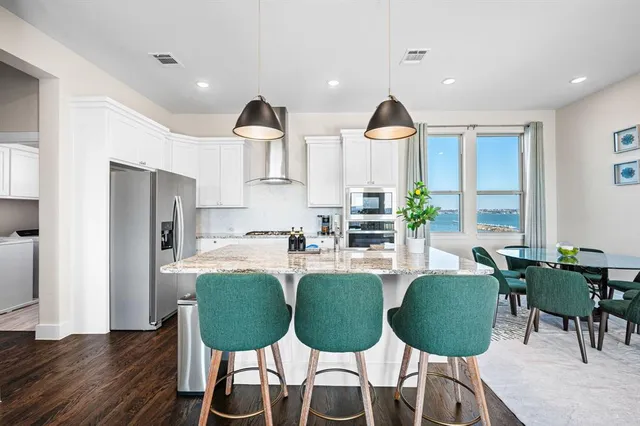 a kitchen with stainless steel appliances kitchen island granite countertop a refrigerator a stove a microwave oven with white cabinets and wooden floor