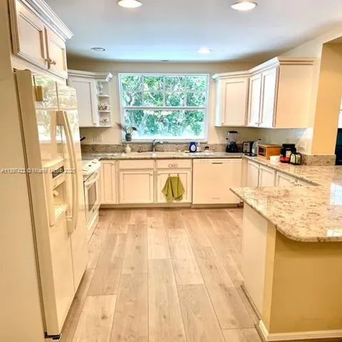 a large white kitchen with a stove a sink and dishwasher a refrigerator with wooden floor