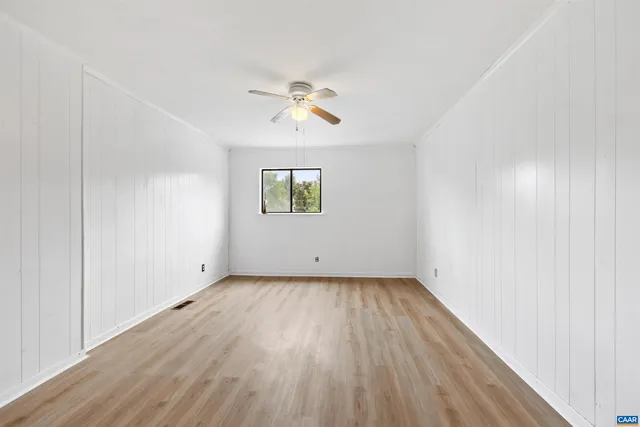 an empty room with wooden floor chandelier fan and windows