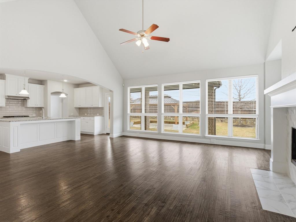 2217 Commons Way Prosper, TX 75078 - Photo 13 of 37 Unfurnished living room with high vaulted ceiling, arched walkways, dark wood finished floors, a fireplace, and ceiling fan