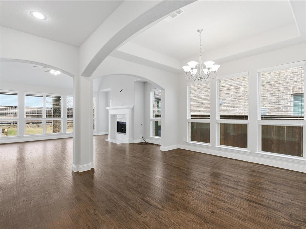 2217 Commons Way Prosper, TX 75078 - Photo 10 of 37 Unfurnished living room featuring a chandelier, a fireplace, a tray ceiling, and arched walkways