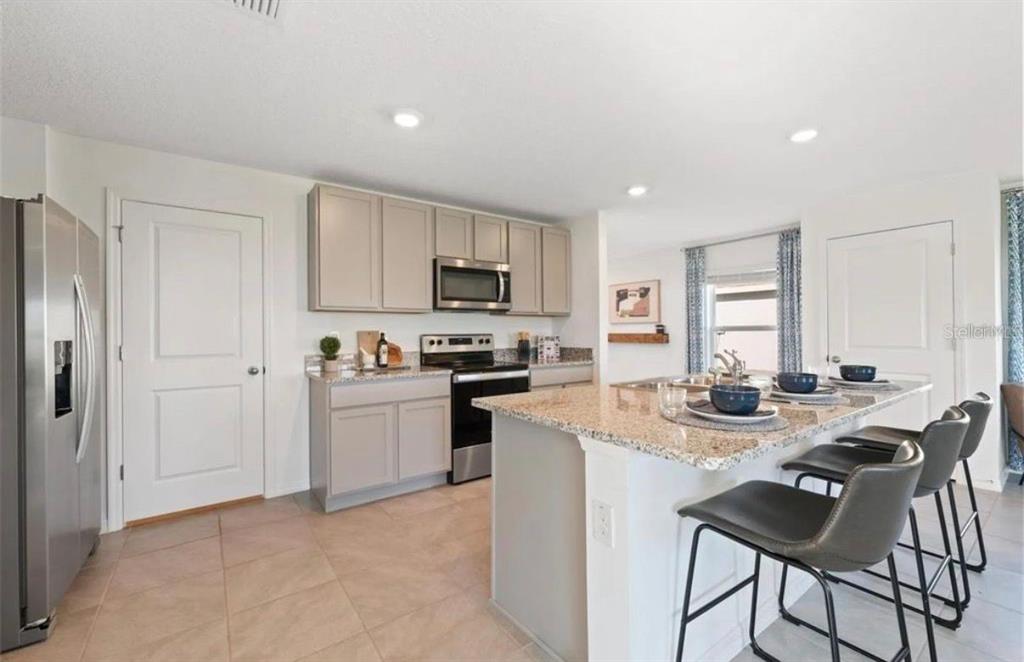 16716 Glacier Bay Loop Wimauma, FL 33598 - Photo 2 of 10 a kitchen with stainless steel appliances kitchen island granite countertop a stove a sink a microwave and a refrigerator