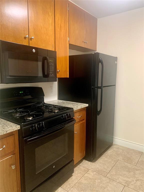 2302 Mesquite Lane, Unit A Georgetown, TX 78628 - Photo 2 of 11 Kitchen featuring black appliances, brown cabinets, light stone countertops, decorative backsplash, and light tile patterned floors