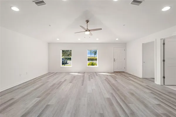 an empty room with wooden floor ceiling fan and windows