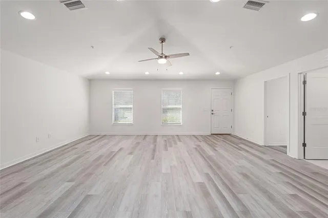 an empty room with wooden floor ceiling fan and windows