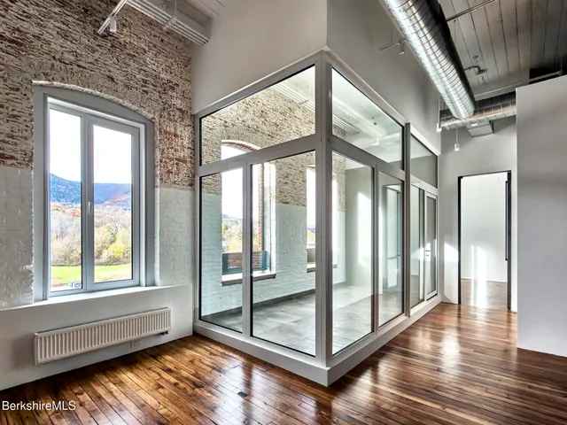 a view of an empty room with wooden floor and windows