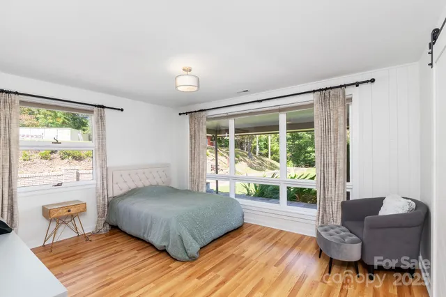 a bedroom with a bed and a large window with wooden floor