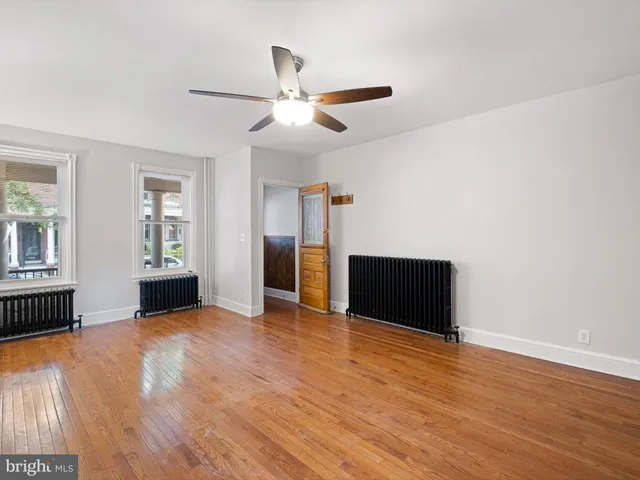 an empty room with wooden floor chandelier fan and windows