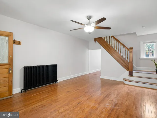 a view of an empty room with wooden floor and a ceiling fan