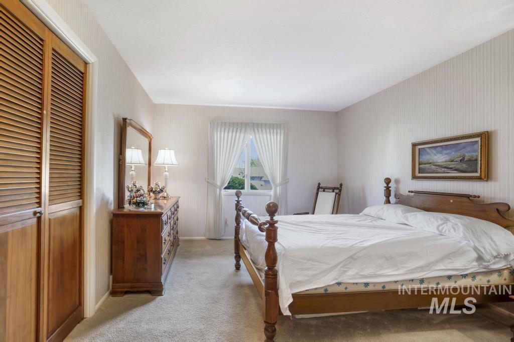 2018 Rancho Vista Drive Twin Falls, ID 83301 - Photo 30 of 50 Carpeted bedroom featuring louvered bi-fold closet doors, a large window with white curtains, and textured wallpaper