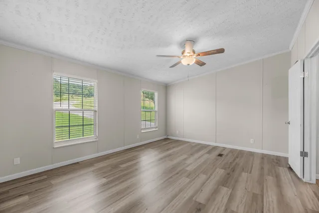 an empty room with wooden floor chandelier fan and windows
