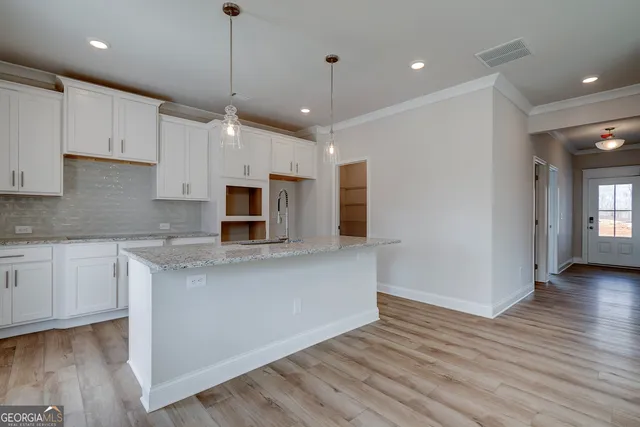 a kitchen with stainless steel appliances granite countertop a refrigerator a sink dishwasher a stove and white cabinets with wooden floor