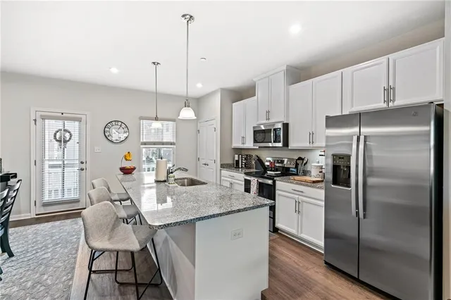 a kitchen with stainless steel appliances granite countertop a refrigerator a sink dishwasher a dining table and chairs with wooden floor