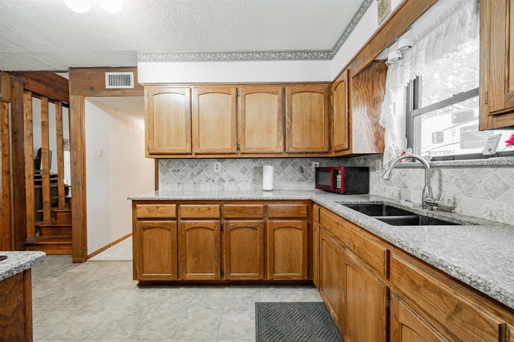 2712 Kleberg Road, Unit B Seagoville, TX 75159 - Photo 5 of 40 Kitchen featuring light stone countertops, a textured ceiling, wood finish cabinets, and tasteful backsplash