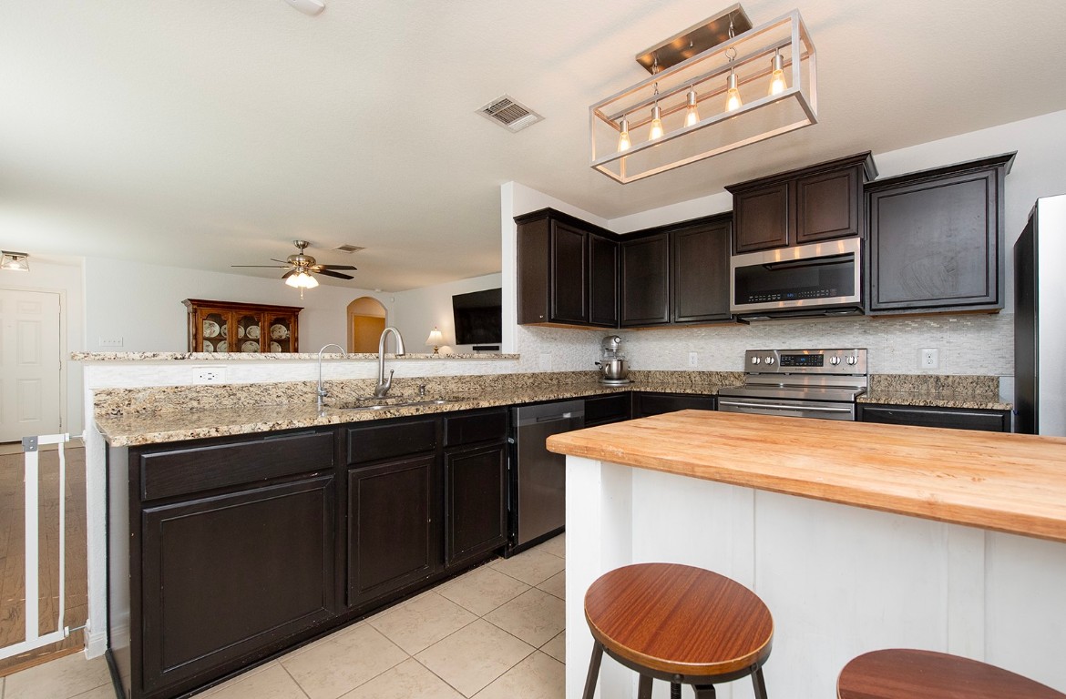 216 Millers Loop Jarrell, TX 76537 - Photo 10 of 31 Kitchen featuring wood counter island, a kitchen breakfast bar, stainless steel appliances, a peninsula, and light tile patterned floors