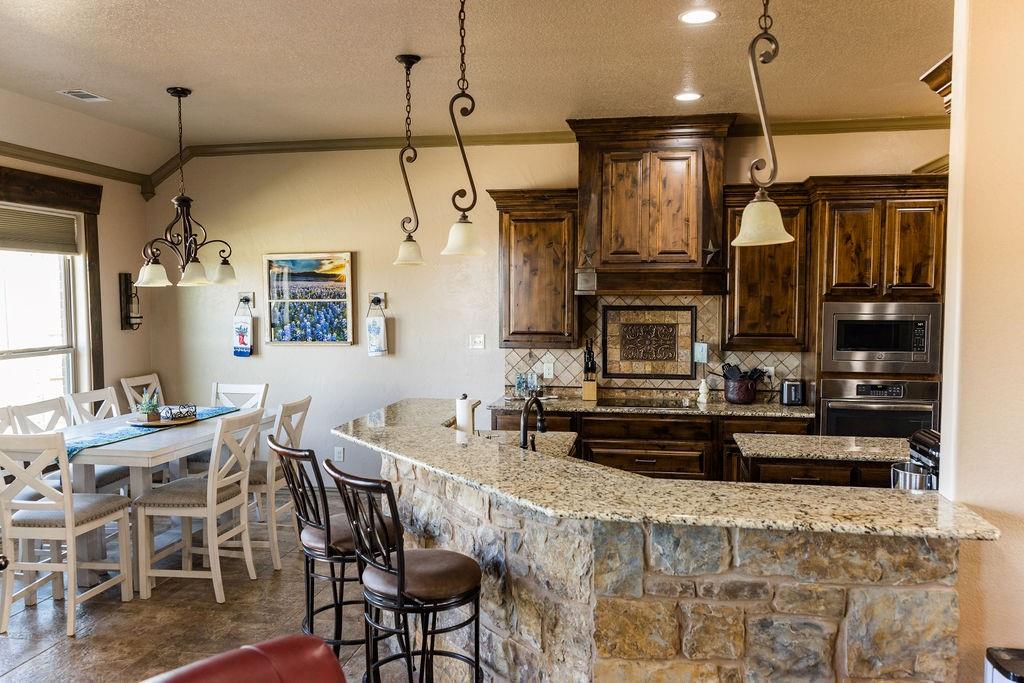 123 Cactus Drive Decatur, TX 76234 - Photo 9 of 30 Kitchen featuring stone-clad breakfast bar, granite countertops, wood cabinetry, stainless steel appliances, and tile backsplash