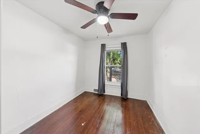 an empty room with wooden floor chandelier fan and windows
