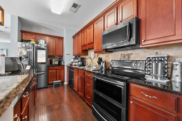 a kitchen with stainless steel appliances granite countertop a refrigerator a stove top oven a sink dishwasher and wooden floor