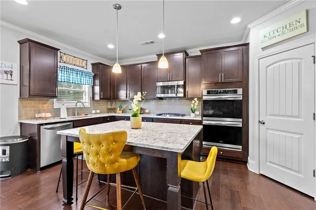 a kitchen with stainless steel appliances granite countertop a refrigerator a sink dishwasher a stove and a dining table with wooden floor