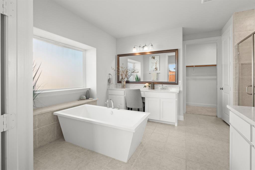 1320 Cartona Road Fate, TX 75087 - Photo 26 of 35 Freestanding soaking tub with tiled surround, dual vanity with undermount sinks, frameless glass shower enclosure, and neutral tile flooring