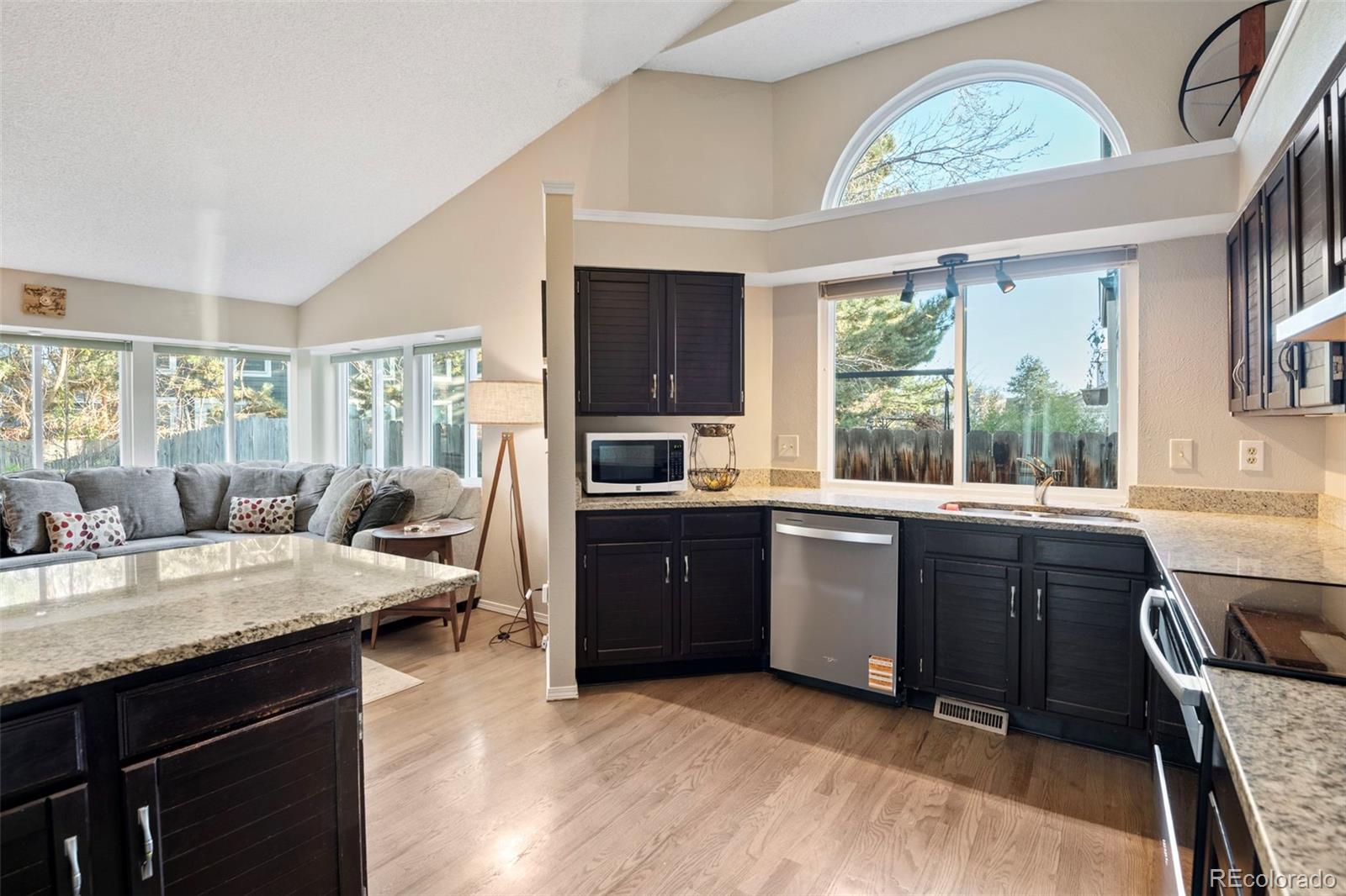 8482 Oak Street Arvada, CO 80005 - Photo 9 of 34 a kitchen with granite countertop a stove a sink dishwasher and a stove top oven with wooden floor