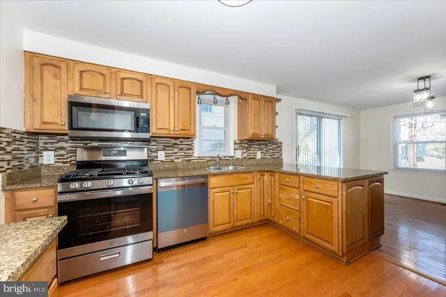 a kitchen with stainless steel appliances granite countertop a stove top oven a sink dishwasher a dining table and chairs with wooden floor