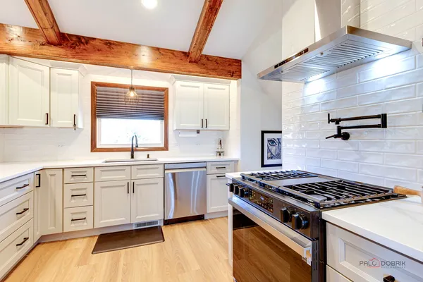 a kitchen with stainless steel appliances a stove a sink dishwasher and white cabinets with wooden floor