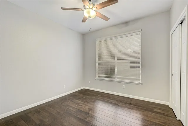 an empty room with wooden floor chandelier fan and windows