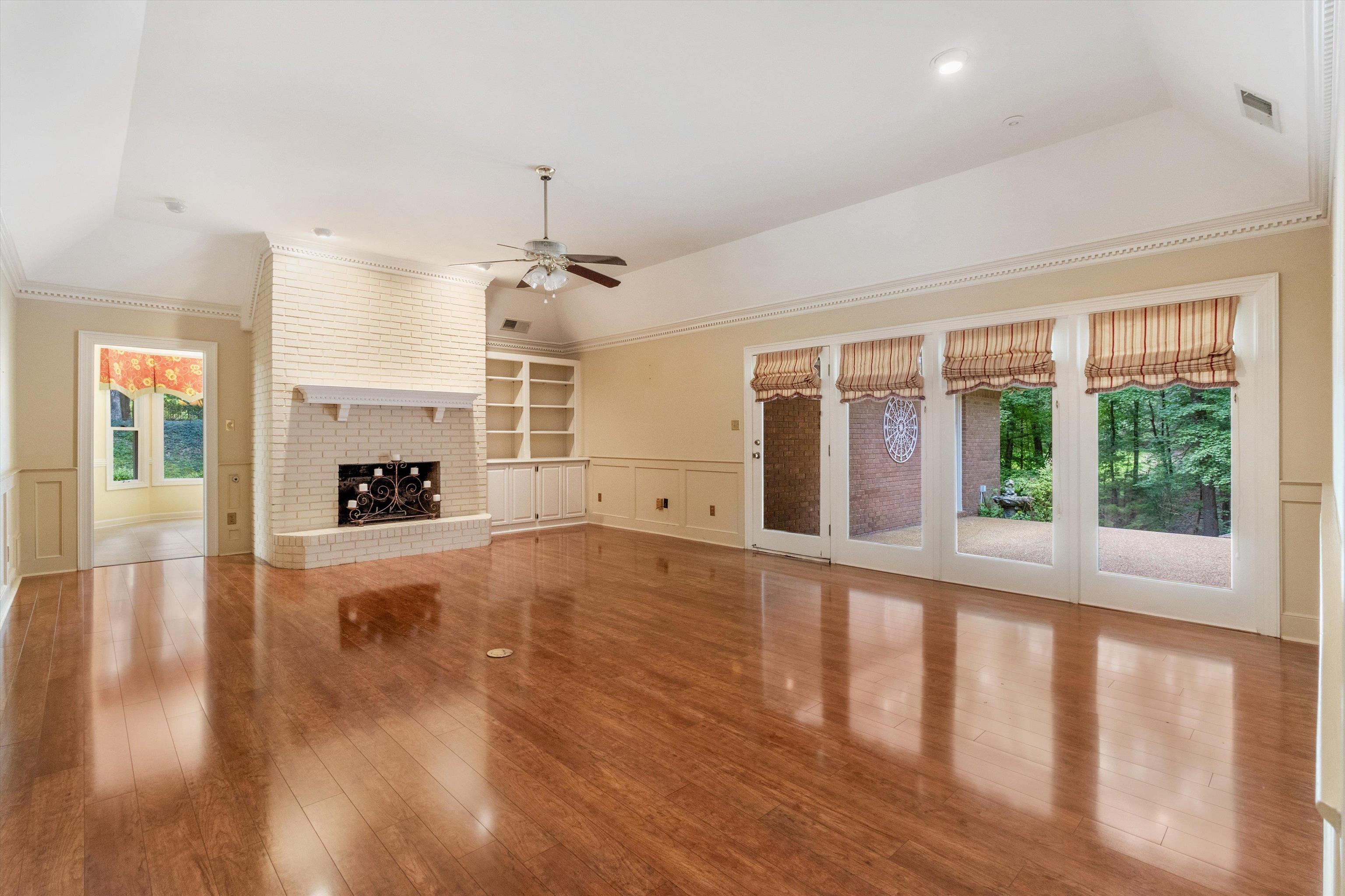 Unfurnished living room with ceiling fan, ornamental molding, wood finished floors, a brick fireplace, and built in features