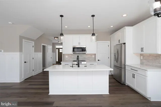 a kitchen with stainless steel appliances kitchen island granite countertop a sink a stove a refrigerator and island with wooden floor