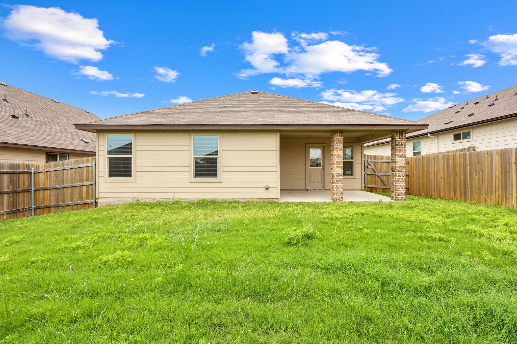 109 Gunther Way Taylor, TX 76574 - Photo 25 of 29 Expansive backyard featuring a covered patio with brick columns, a wood fence enclosing the property, and beige siding on the exterior