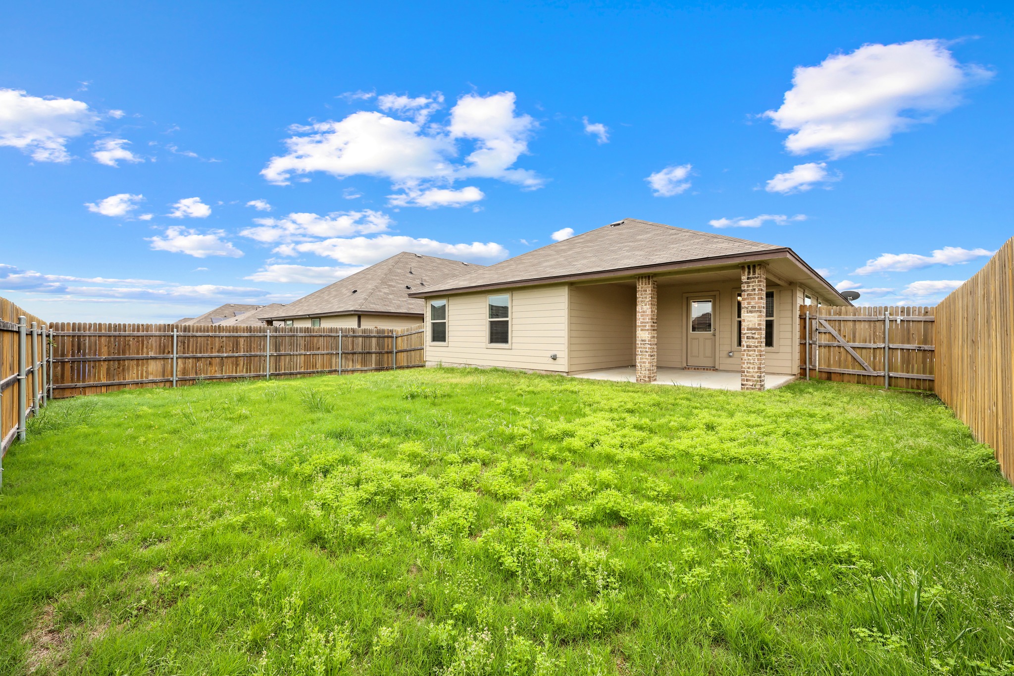 109 Gunther Way Taylor, TX 76574 - Photo 28 of 29 Expansive backyard featuring a covered concrete patio, full wood privacy fencing, and a light-colored siding exterior with brick pillar accents