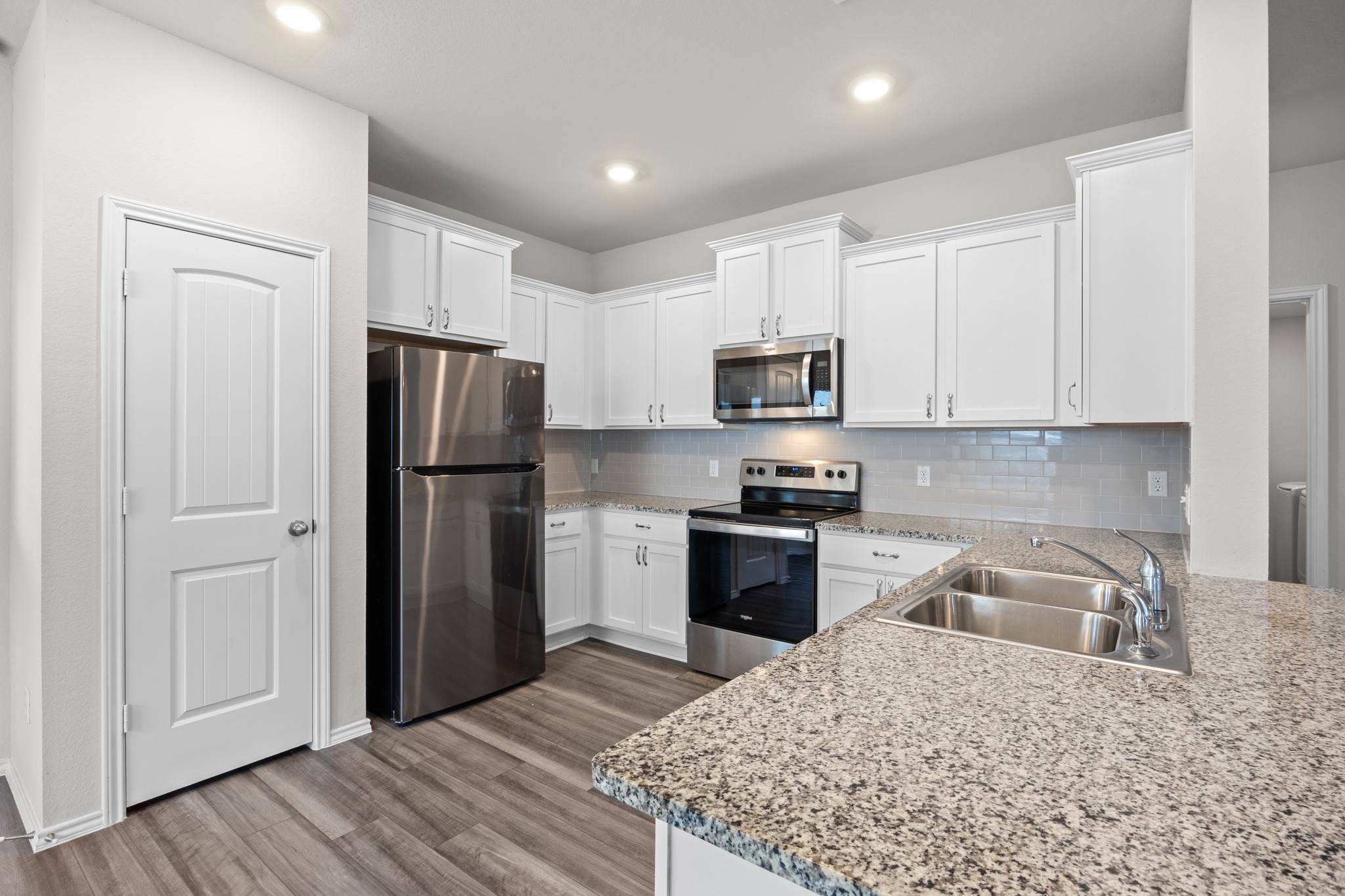 109 Gunther Way Taylor, TX 76574 - Photo 8 of 29 Modern kitchen featuring white cabinetry, stainless steel appliances, speckled stone countertops, a tile backsplash, and wood-look LVP flooring.