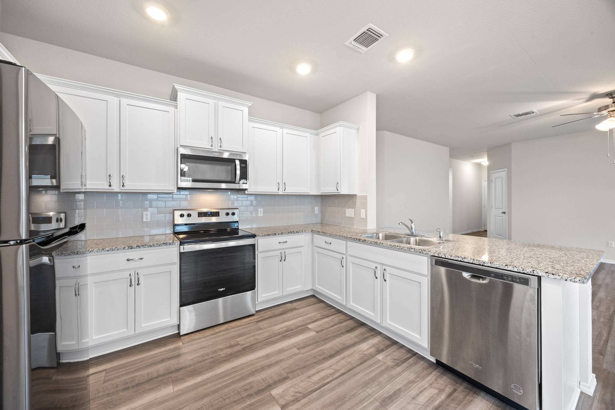 109 Gunther Way Taylor, TX 76574 - Photo 9 of 29 Kitchen featuring white cabinetry, stainless steel appliances, speckled countertops, a subway tile backsplash, and wood-finish flooring