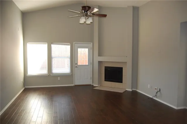 an empty room with wooden floor fan and windows