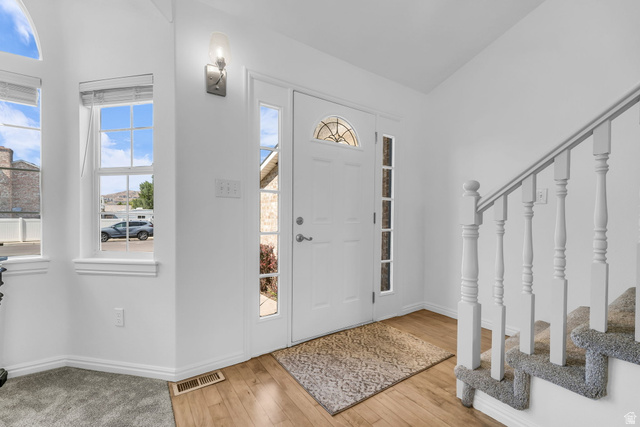 1147 West State Road Lehi, UT 84043 - Photo 2 of 31 Bright entryway featuring a white paneled door with an arched decorative glass insert and sidelights, wood-finish flooring, a wall-mounted sconce, and a carpeted staircase with white balusters