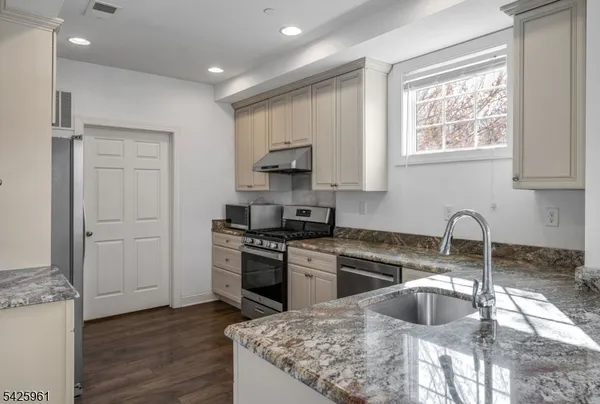 a kitchen with granite countertop a stove a sink and a refrigerator