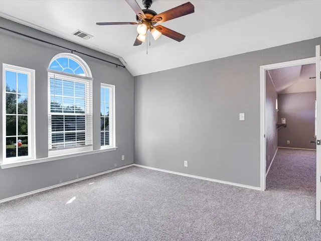 an empty room with chandelier fan and windows