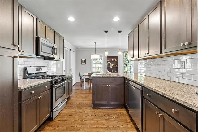 a kitchen with stainless steel appliances granite countertop a sink a stove top oven a refrigerator with wooden cabinets and floor