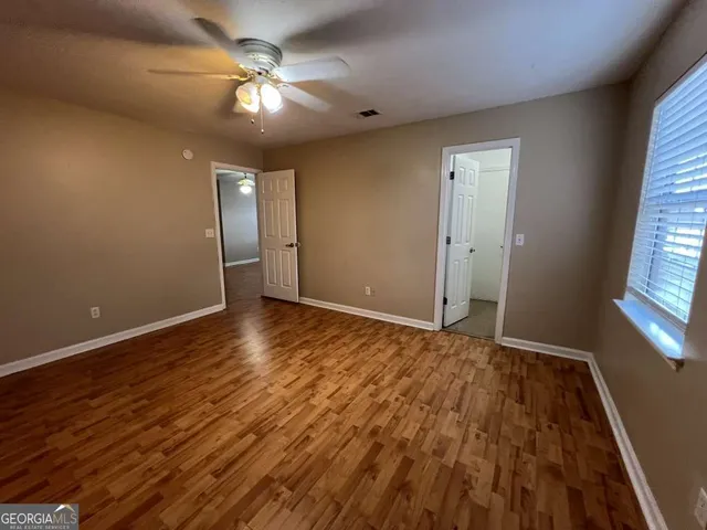 an empty room with wooden floor chandelier fan and windows