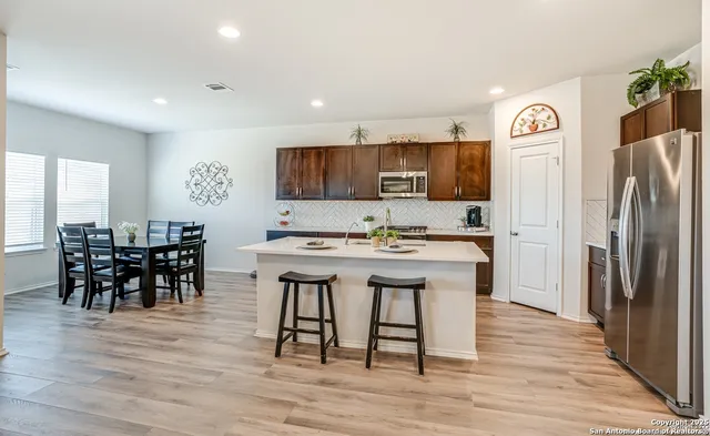 a kitchen with stainless steel appliances granite countertop a dining table chairs refrigerator and microwave