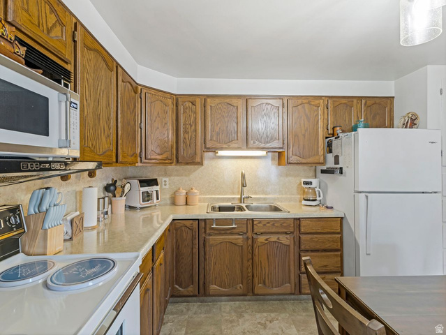 1502 North 475 West Sunset, UT 84015 - Photo 9 of 23 Kitchen featuring wood cabinetry, solid surface countertops, double basin sink with gooseneck faucet, built-in microwave, and white appliances