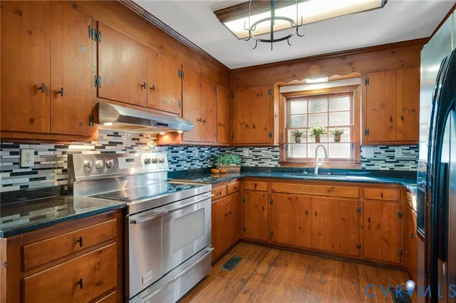 a kitchen with stainless steel appliances granite countertop wooden cabinets a sink a stove a dining table and chairs with wooden floor