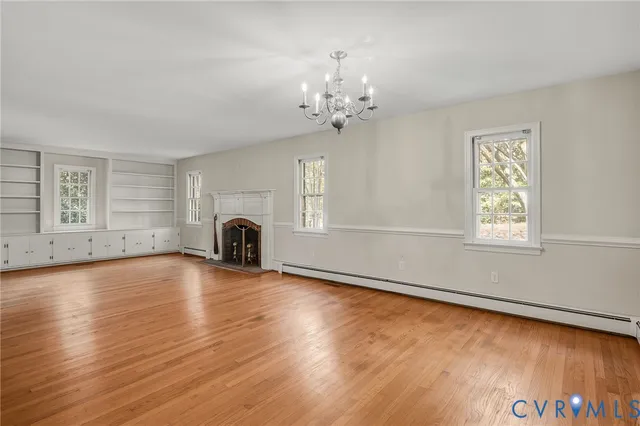 an empty room with wooden floor chandelier and windows