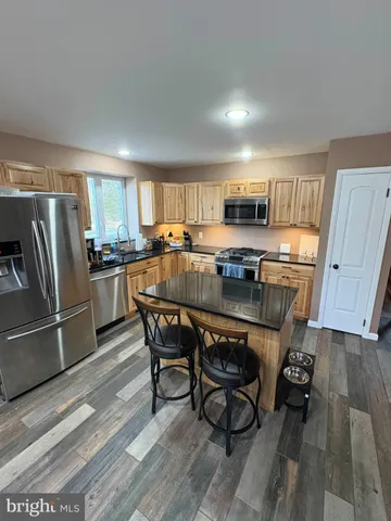 a kitchen with stainless steel appliances granite countertop a stove a refrigerator a sink a dining table and chairs with wooden floor