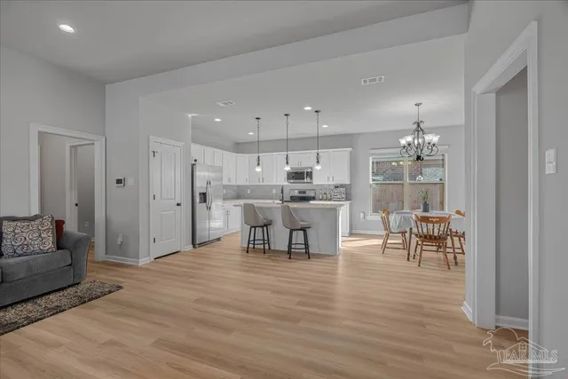 a kitchen with stainless steel appliances granite countertop a sink a refrigerator a stove a kitchen island and chairs with wooden floor