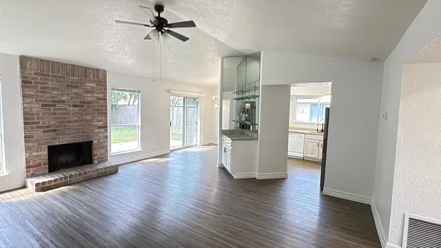 an empty room with wooden floor fireplace and windows