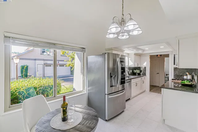 a kitchen with stainless steel appliances granite countertop a refrigerator a sink dishwasher a dining table and chairs with wooden floor