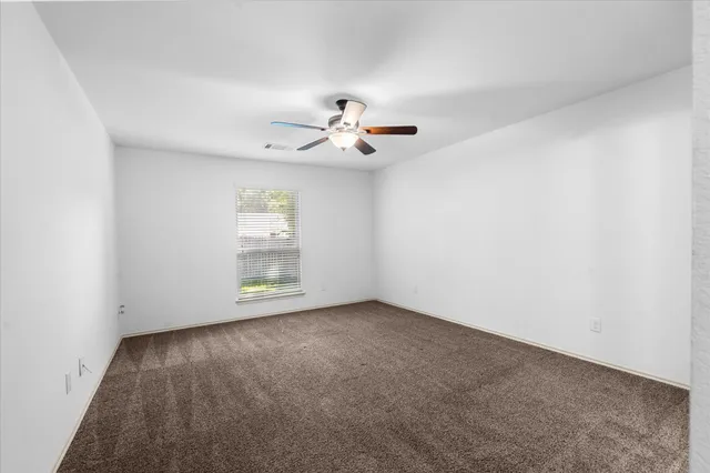 an empty room with chandelier fan and windows